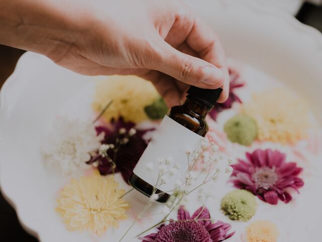 hand holds little oil bottle in front of flowers on a plate